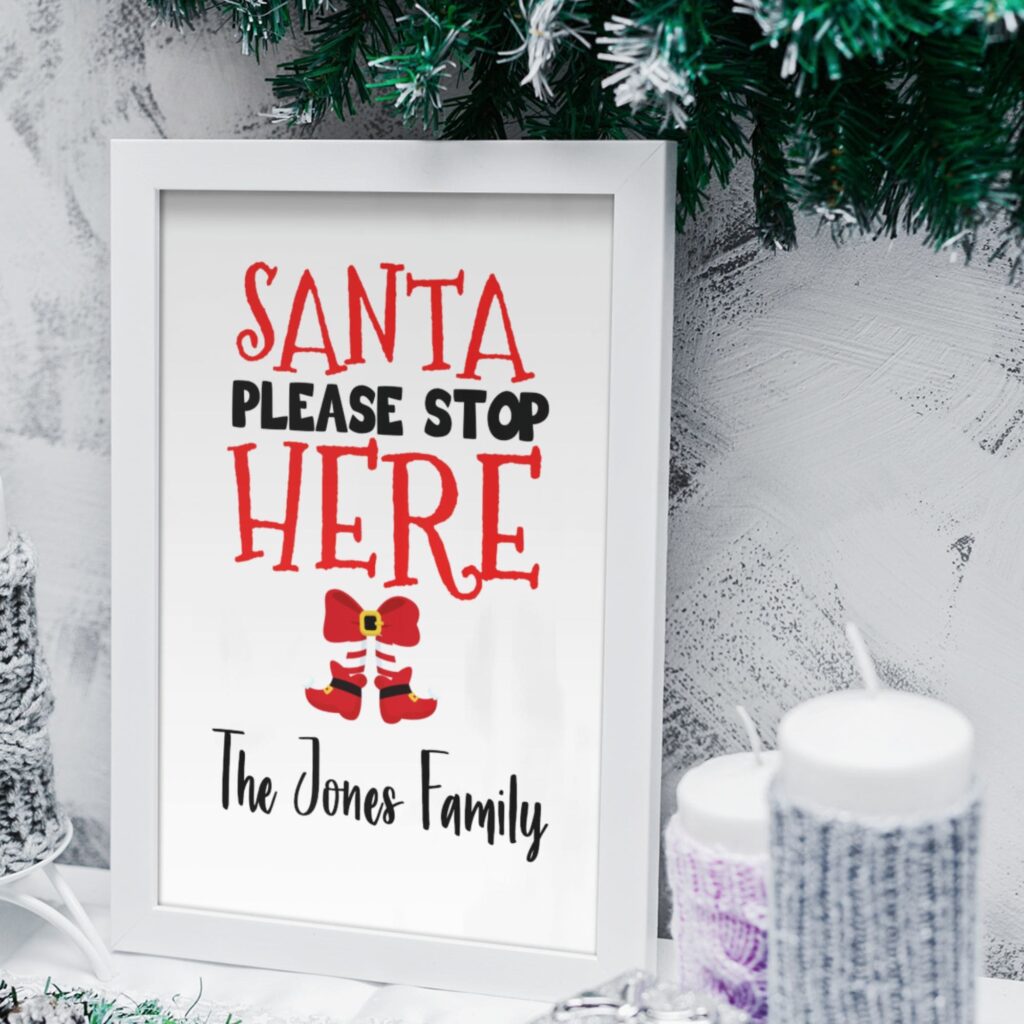 Santa stop here sign in a white frame with some christmas decoractions