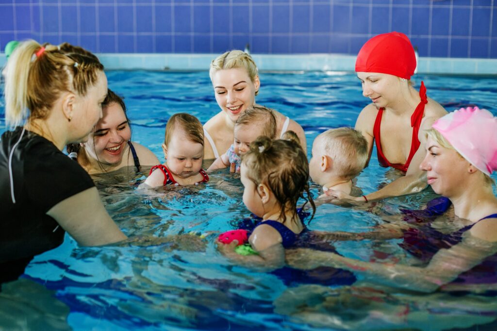 Group of mothers with little babies in children's swimming section with coach. Healthy lifestyle.